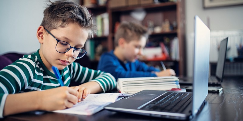 Two students doing schoolwork in workbooks with laptops beside them