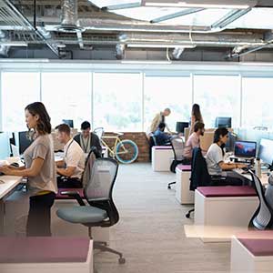 An open office with a wall of windows and a row of different desks (standing sitting, etc.)