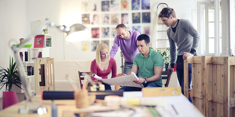 Three men and a woman sitting around looking at a paper. 