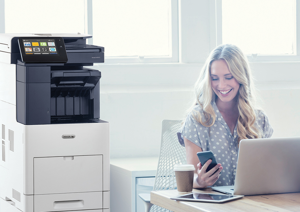 Happy woman with smartphone and laptop, sitting next to a Xerox MFP