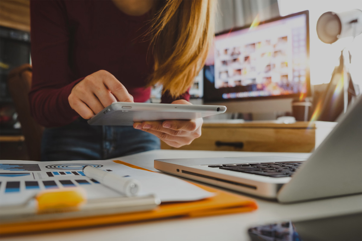 Woman using her tablet at desk with laptop