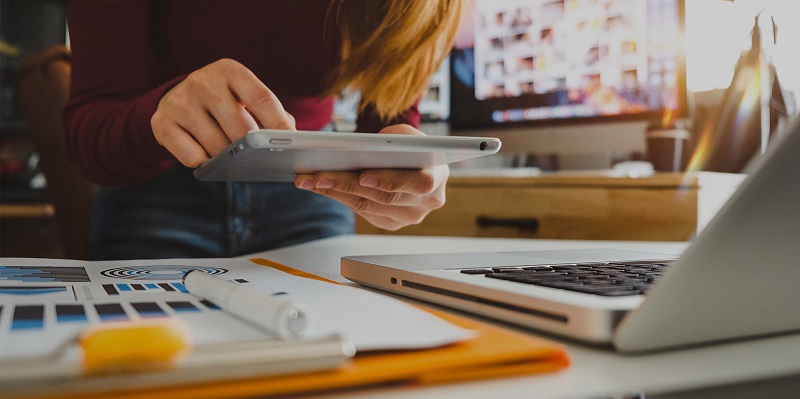 Woman using her tablet at desk with laptop