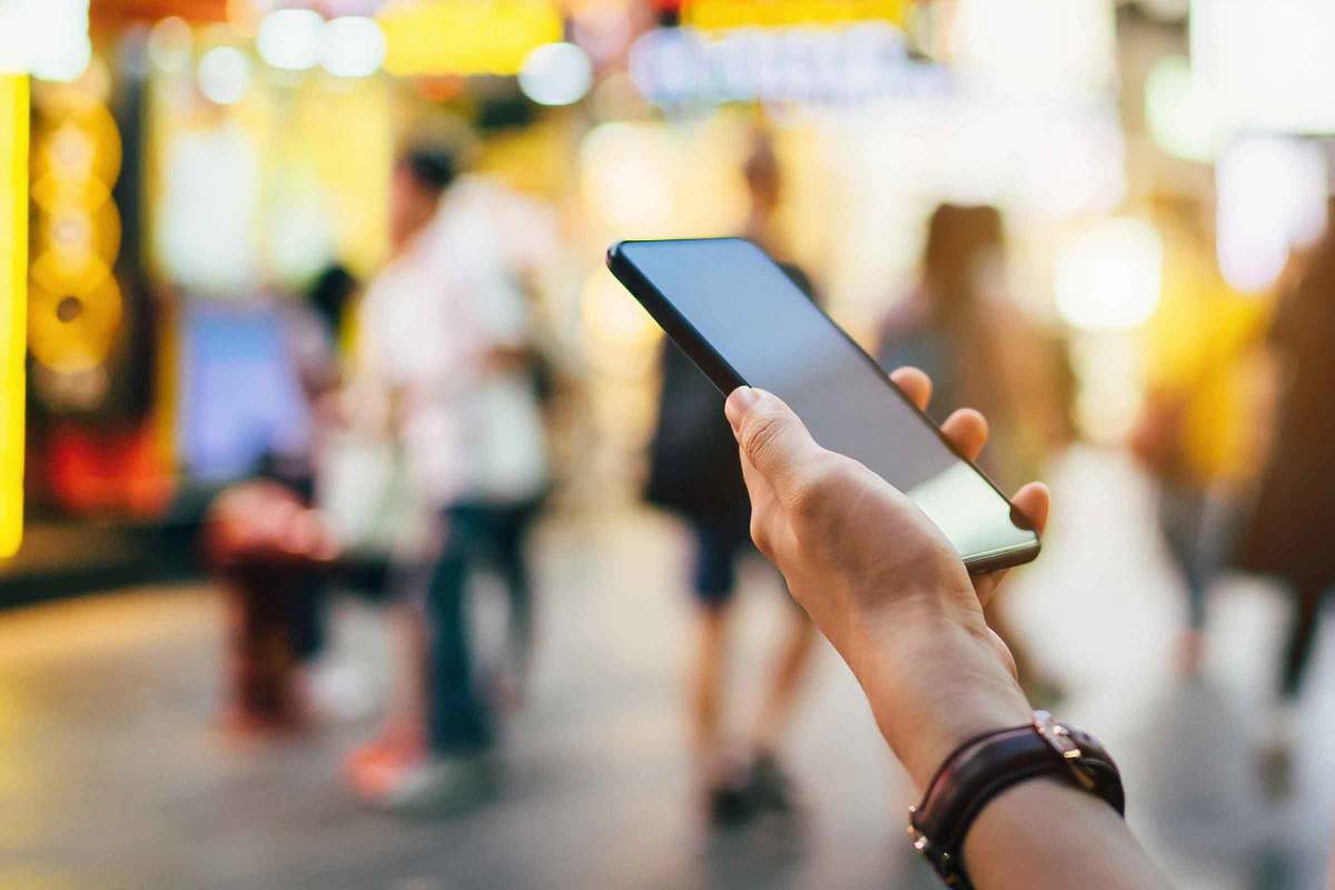A hand holding a smartphone, with a blurred crowd in the background