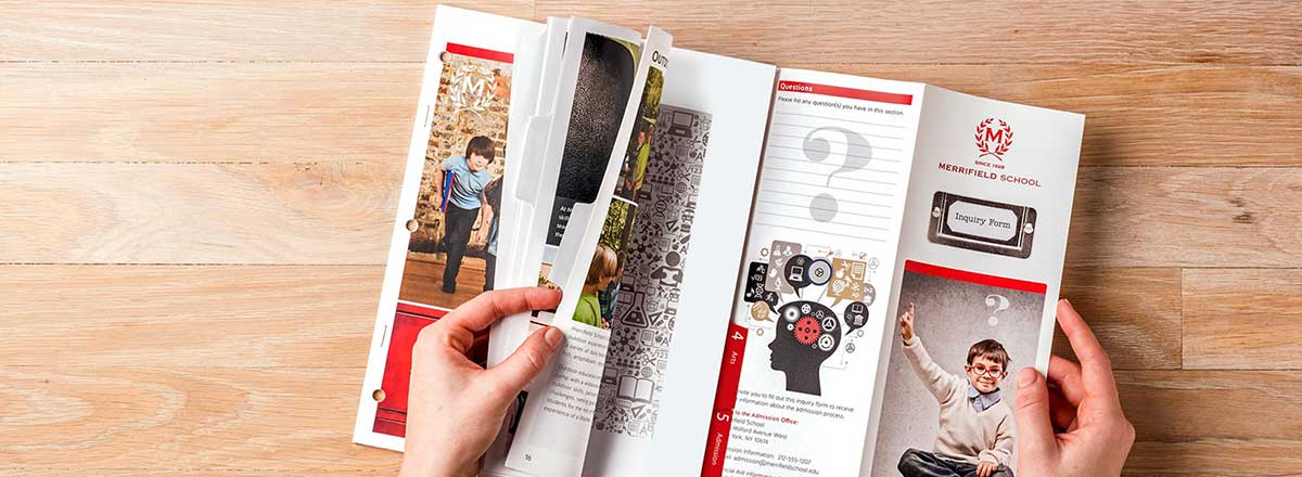 Hands holding a folded brochure over a wooden table