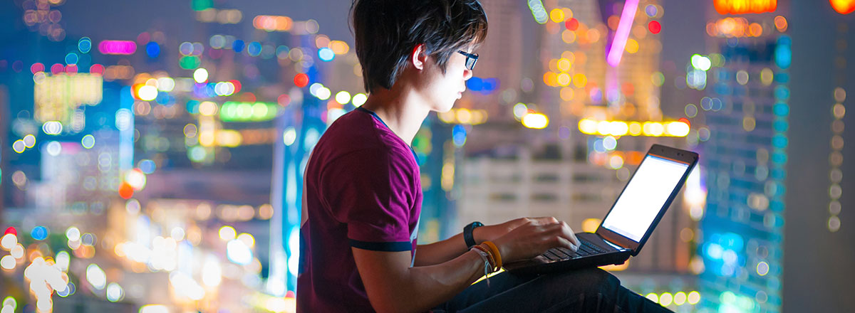 Young man using a laptop with a night time cityscape in the background