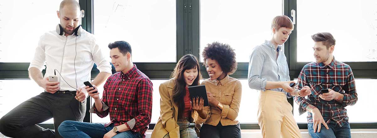 Young professionals in front of a row of windows, looking at mobile devices together