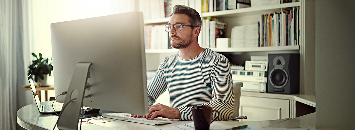 A man in a home office working on a computer with a cup of coffee