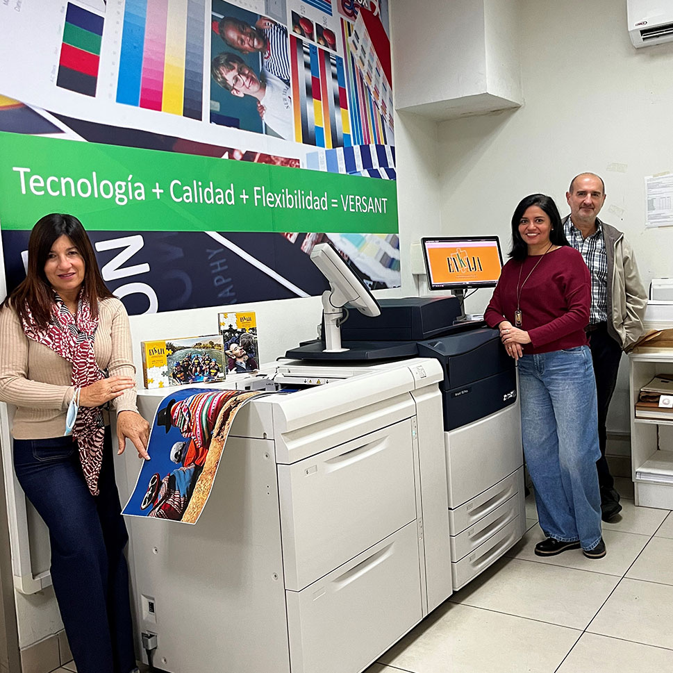 Staff of IMPRESSO Gráfica with their Xerox Versant 180 Press. A sign behind them says "Tecnología + Calidad + Flexibilidad = VERSANT".