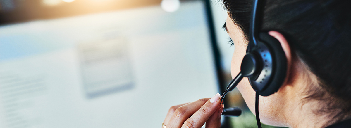 A woman speaking into a headset and looking at a computer