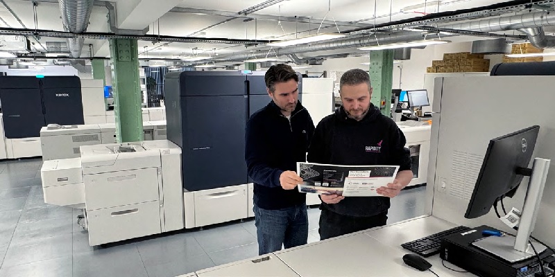 Two employees at Rapidity review print samples from their Xerox Iridesse Production Press