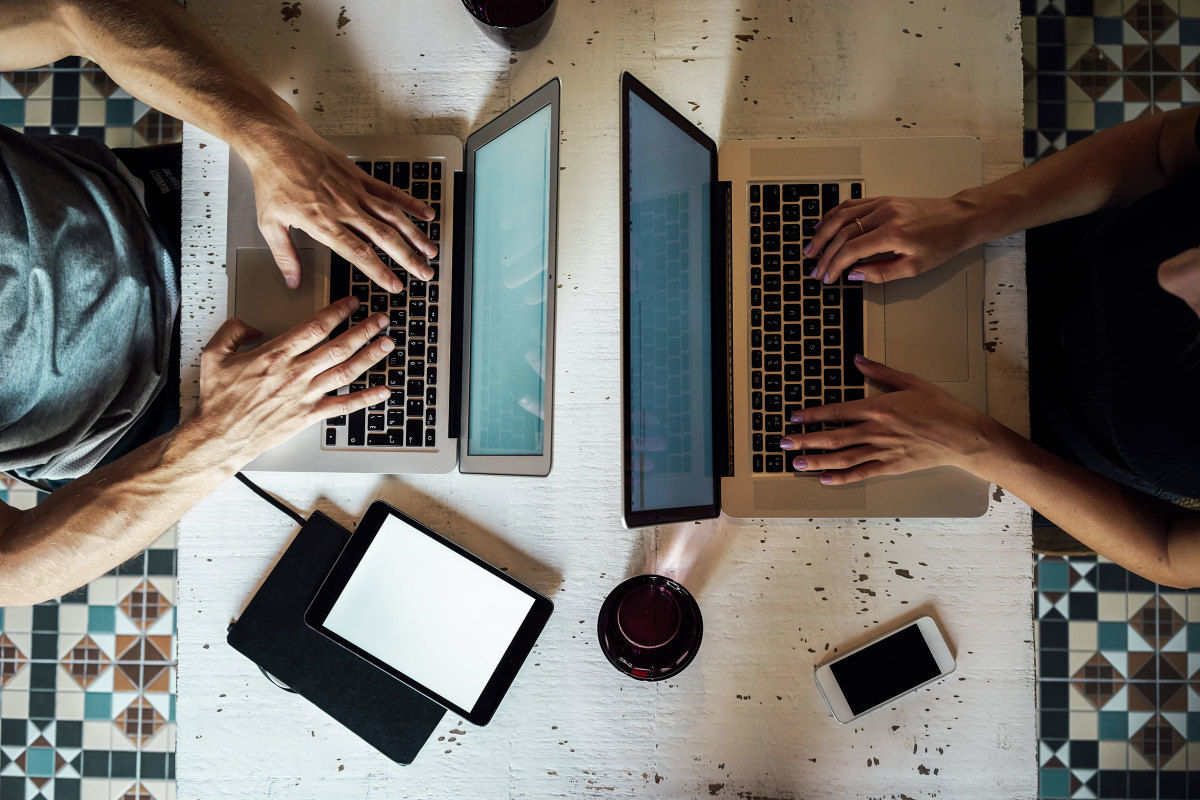 Overhead view of a table with two people working on laptops, next to two tablets and a smartphone