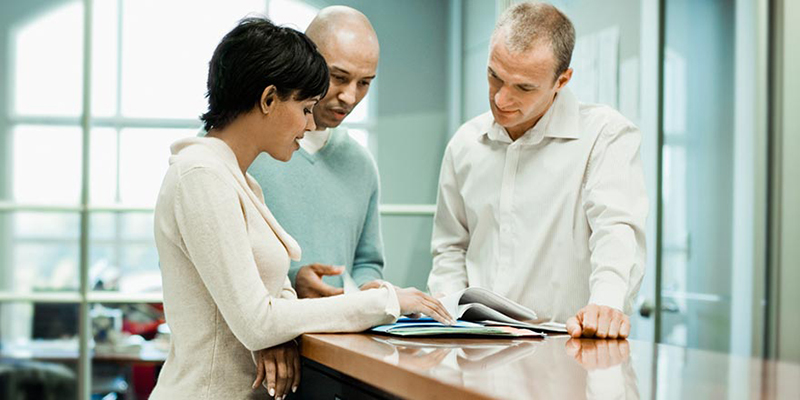 3 coworkers standing at a table looking at a printed report