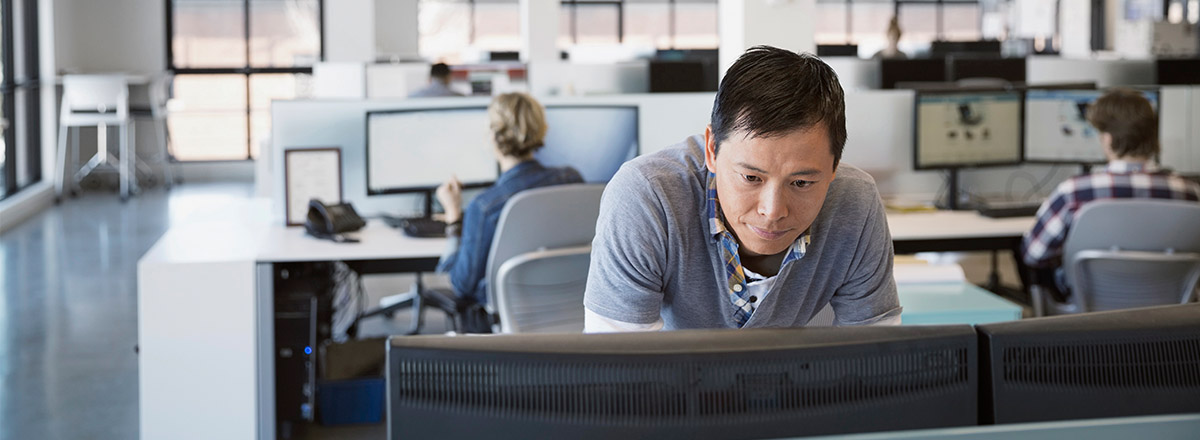 Man in an office looking at two computer monitors side by side