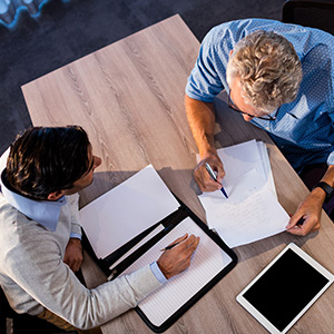 Two men sitting at a desk writing on paper.