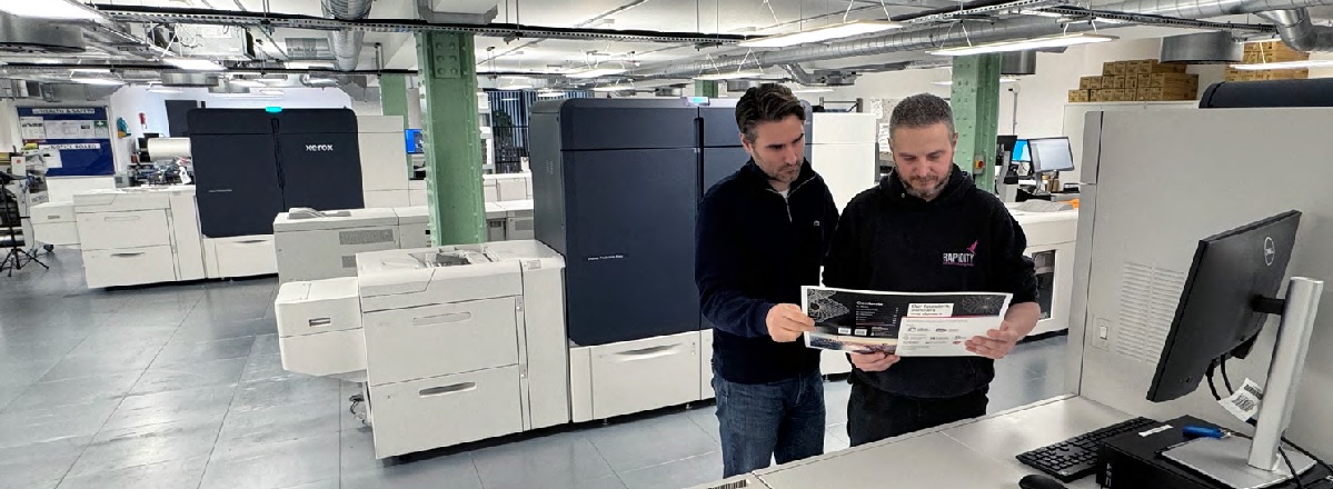 Two employees at Rapidity review print samples from their Xerox Iridesse Production Press