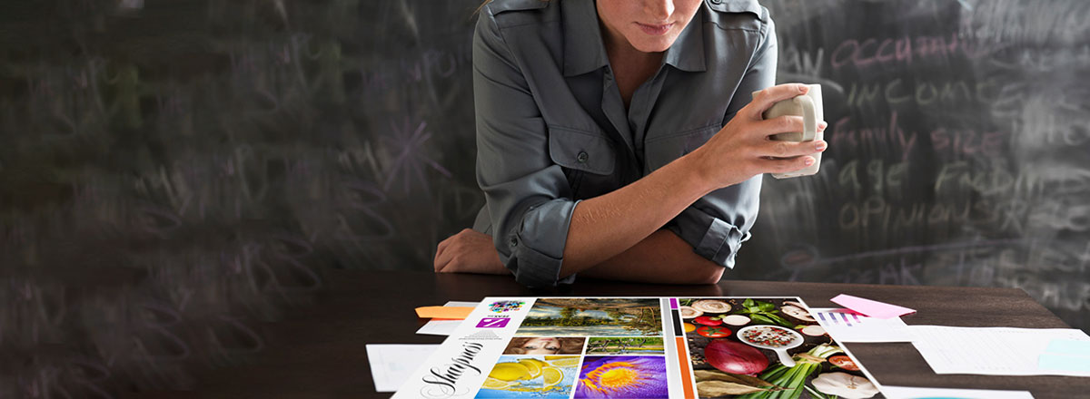 Woman with coffee, in front of a chalkboard, looking at a table covered with colorful print samples