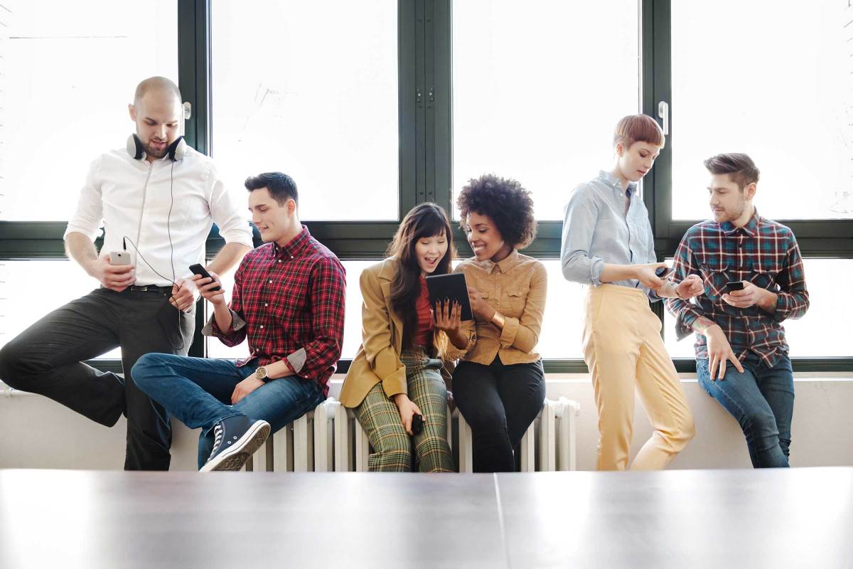 Young professionals in front of a row of windows, looking at mobile devices together