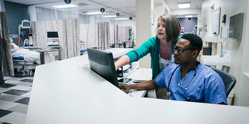 Médecin et infirmière examinant des dossiers numériques des patients, dans une aile d'hôpital.