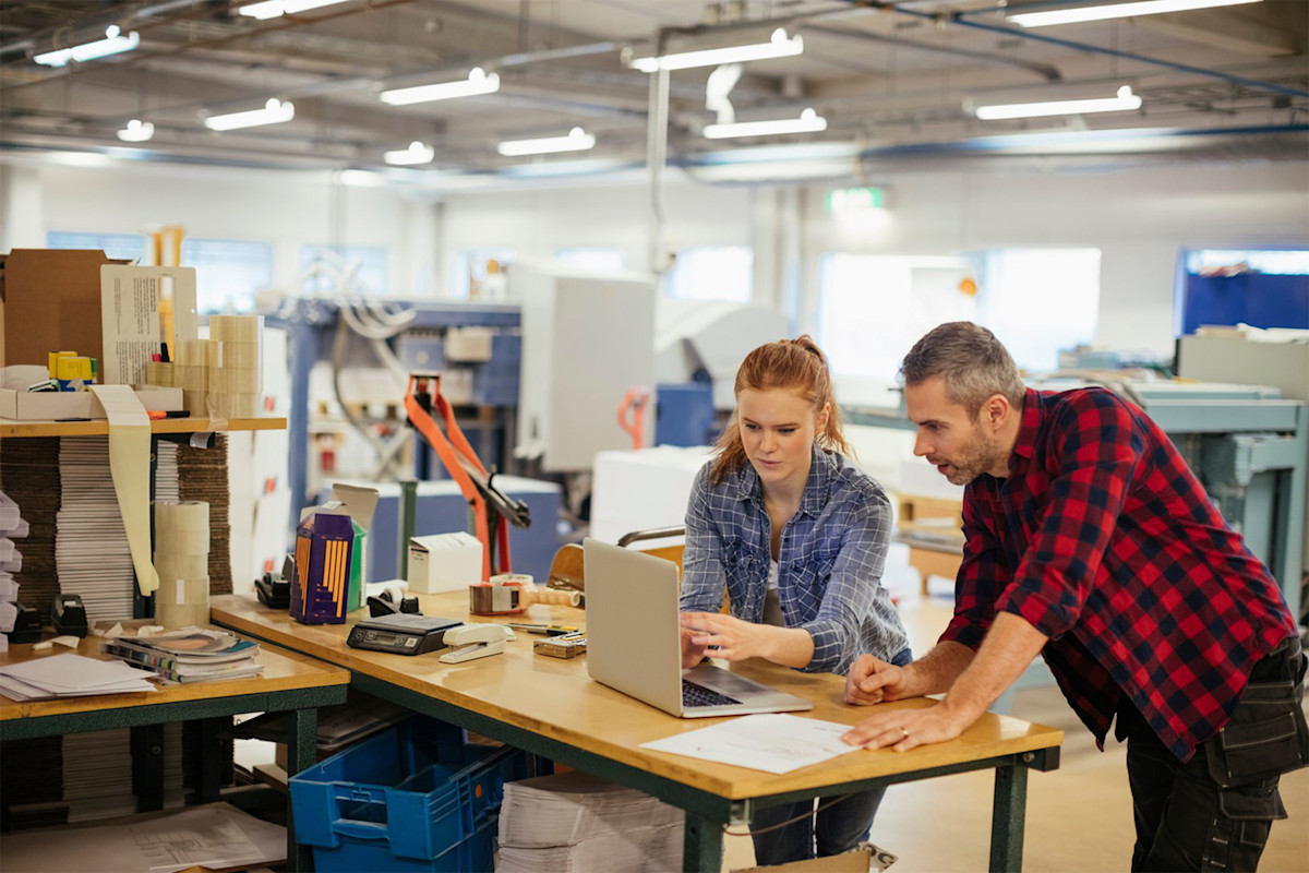 Man and woman standing at a desk looking at a computer screen.
