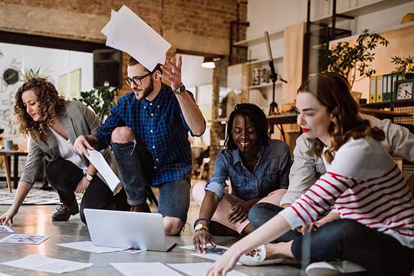 A group of young professionals working together creatively, sitting on the floor, throwing papers