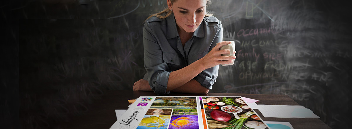 Woman with coffee, in front of a chalk board, looking at a table covered with print samples