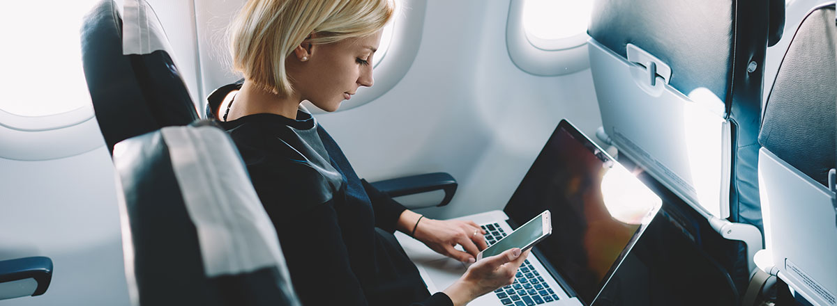 Woman on a plane, using her smart phone and laptop