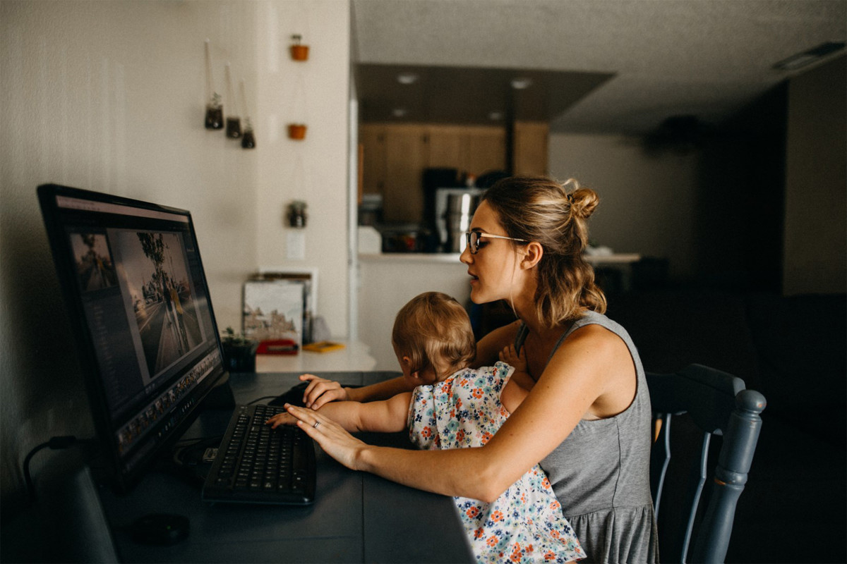 Woman sitting at desk, on her computer in her house with her child on her lap. 