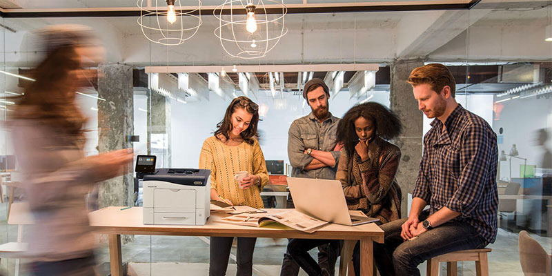young professionals sitting at a modern office desk with xerox versalink c400 printer