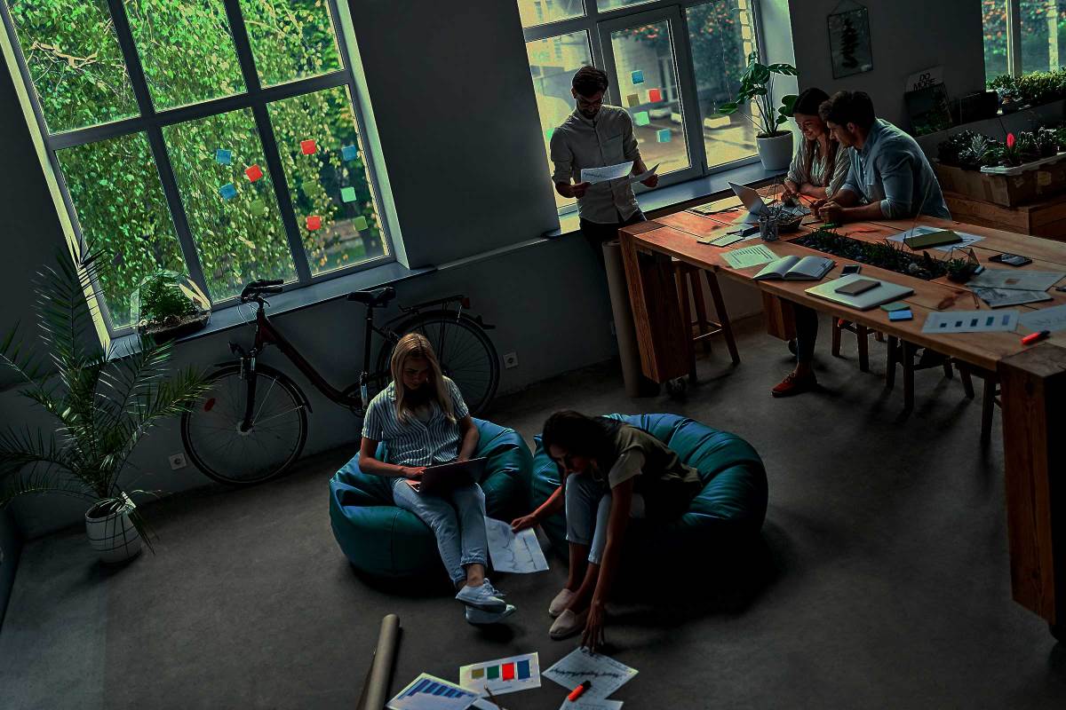 People working in a brightly lit office, sitting in beanbag chairs in front of a bicycle, with several plants in the office