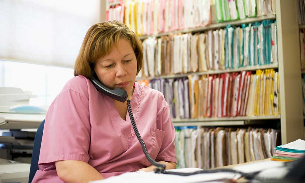 Nurse speaking on the telephone, in front of a bookcase full of colorful file folders