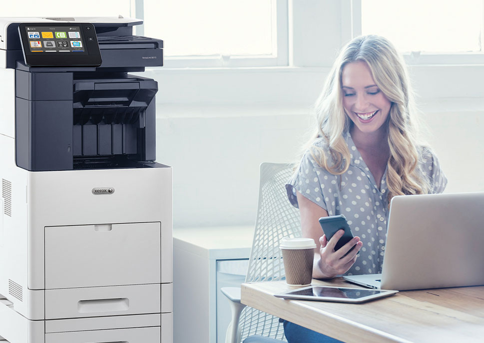 Woman with mobile phone and laptop, next to Xerox MFP