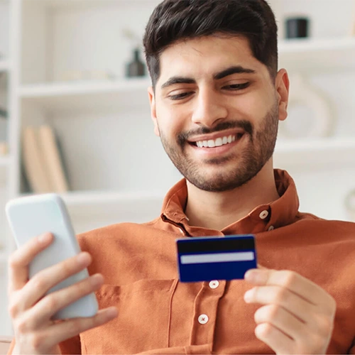 A man holds a debit card while looking at a mobile phone. 