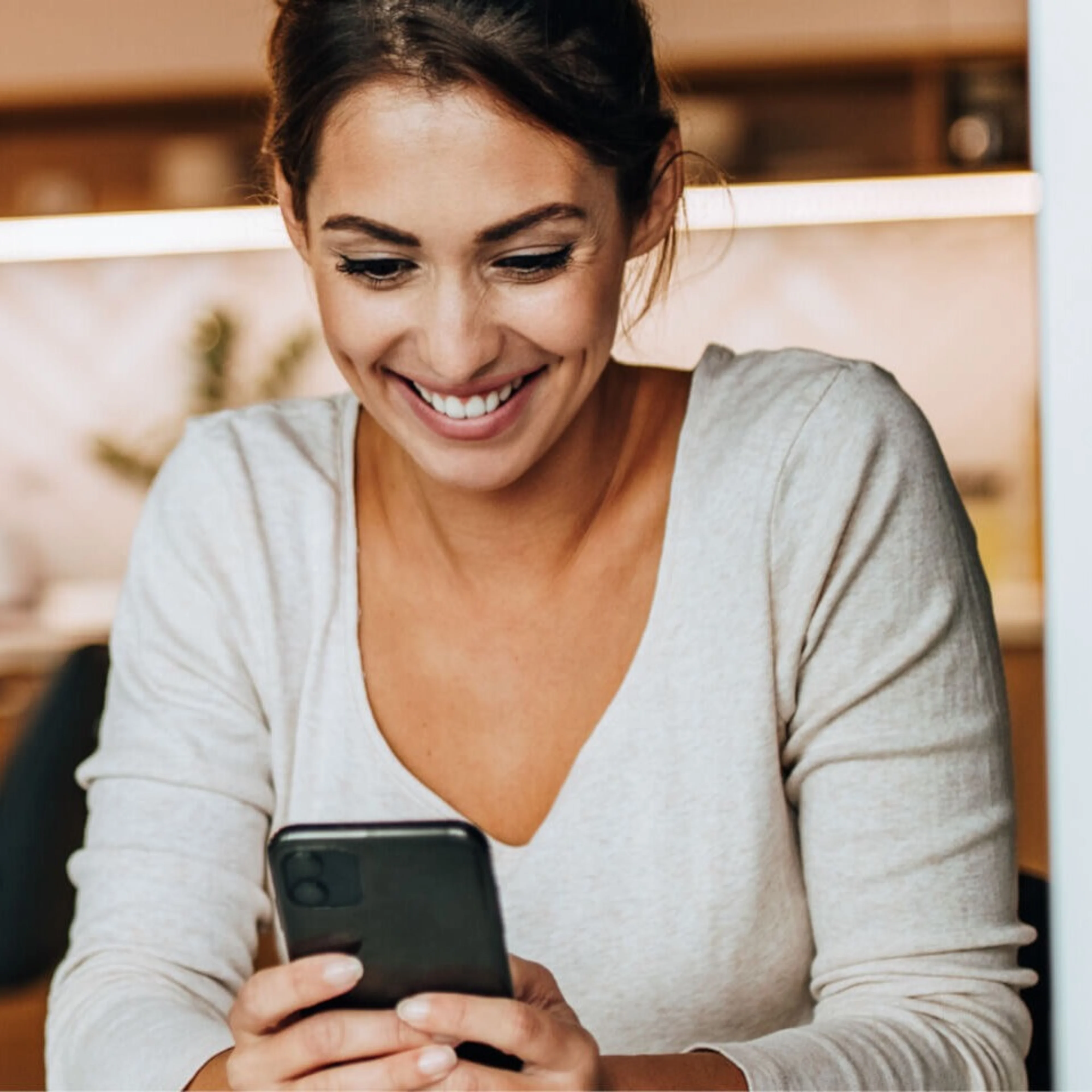 Girl sitting at table smiling at phone white long sleeve v-neck