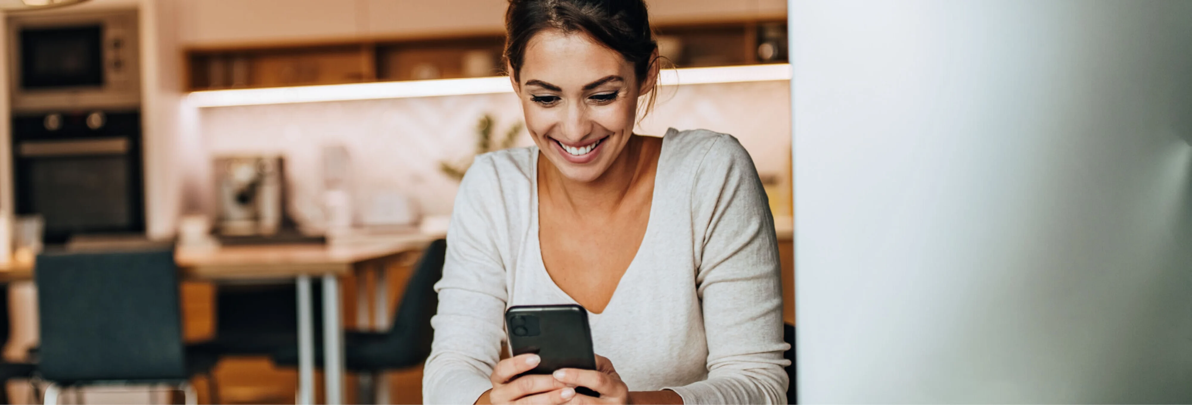 Girl sitting at table smiling at phone white long sleeve v-neck