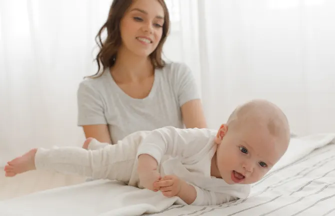 Baby in Bauchlage auf dem Bett mit seiner Mutter.