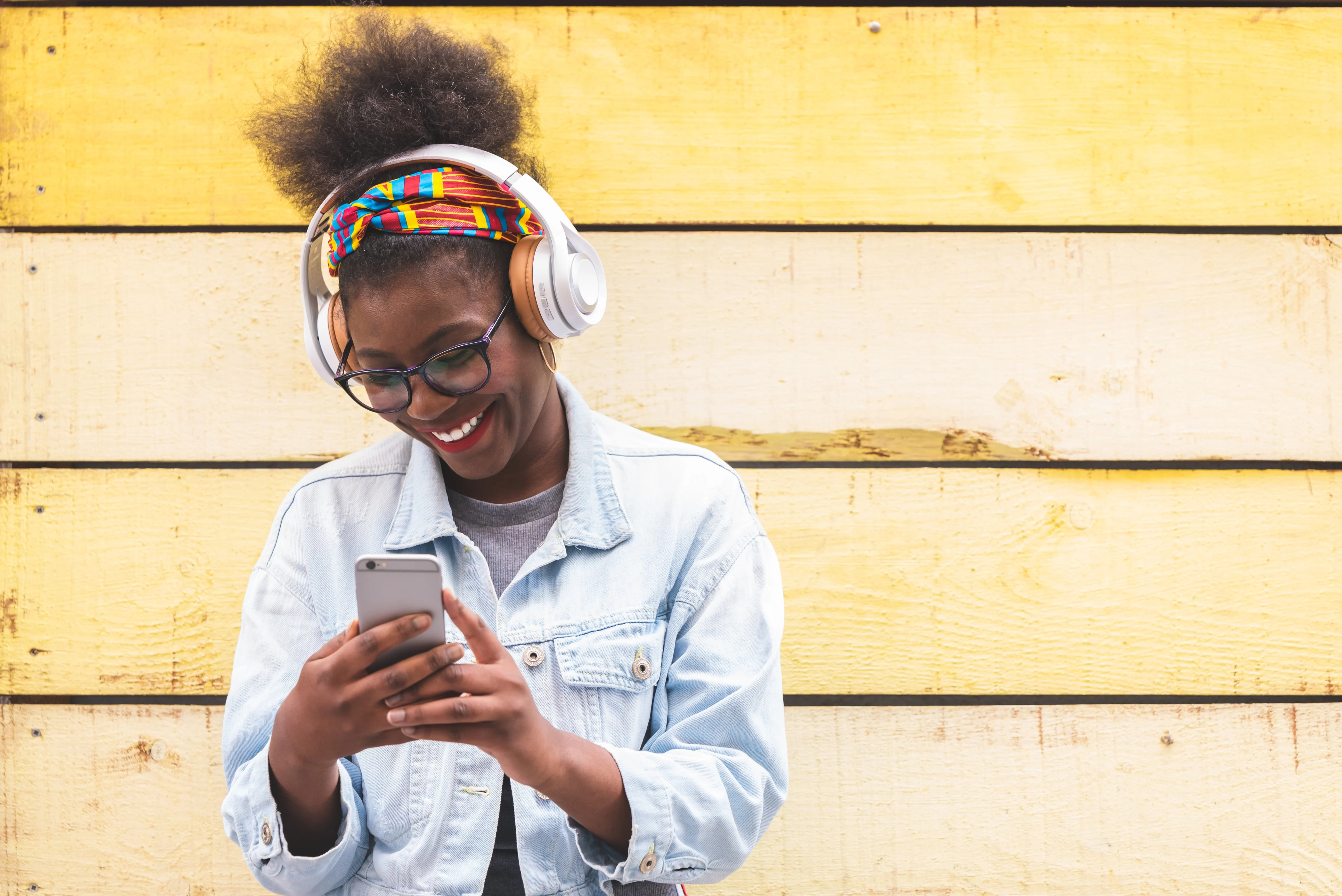 Girl with headphones in front of a pale yellow wall