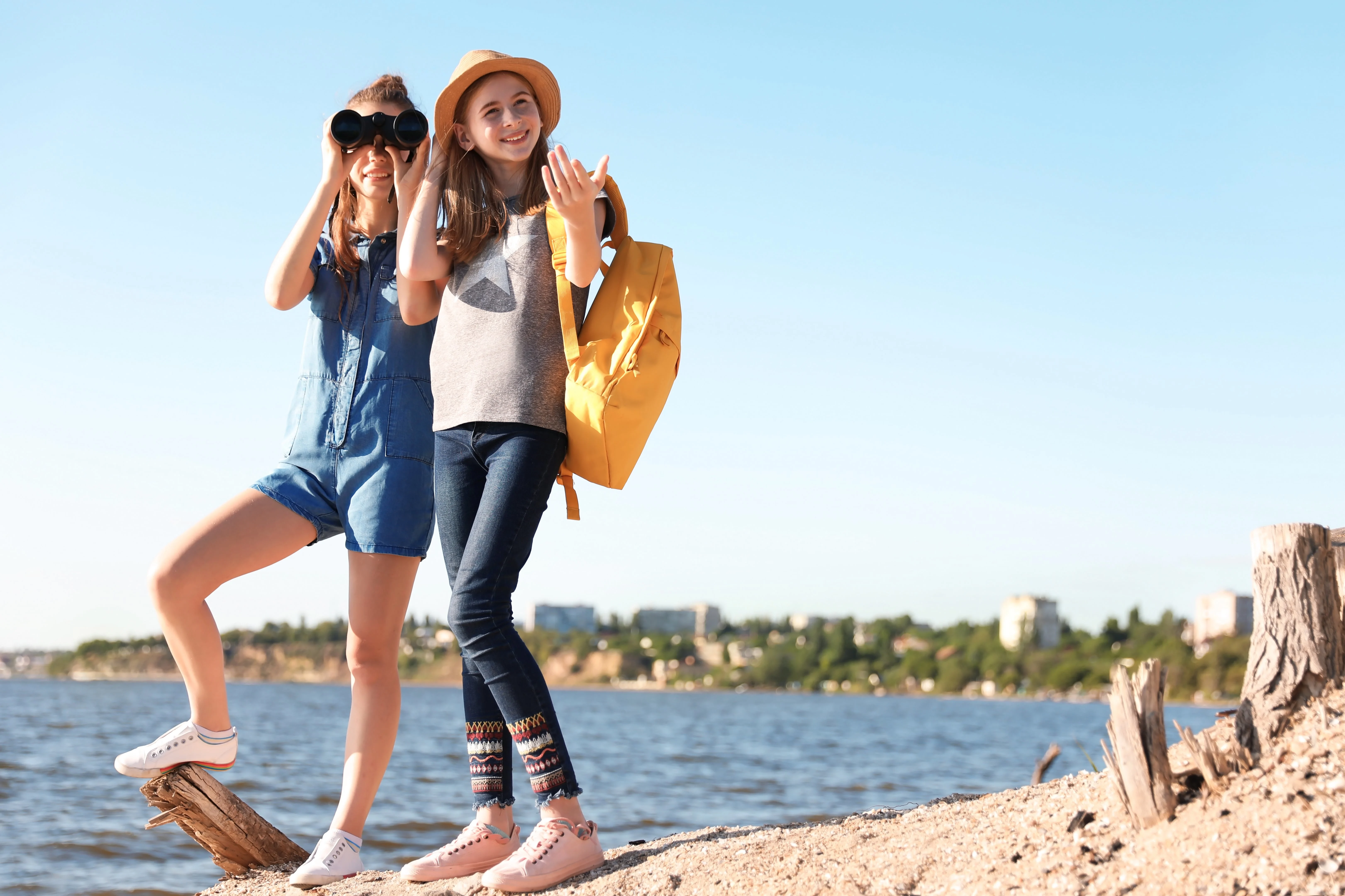Two girls on the seashore standing while one is looking through binoculars