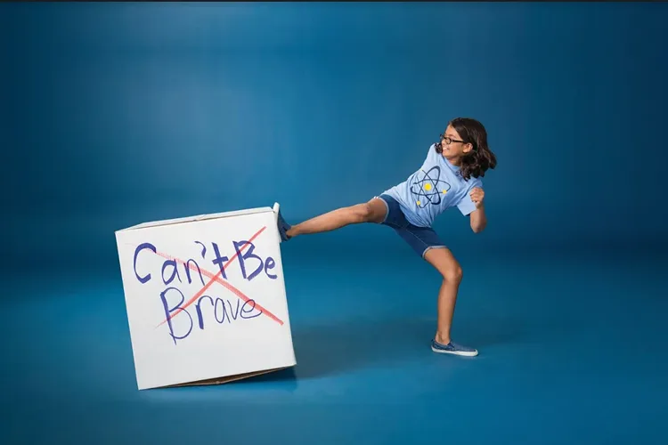 Girl kicking a cardboard box that has "Can't be brave" written on it
