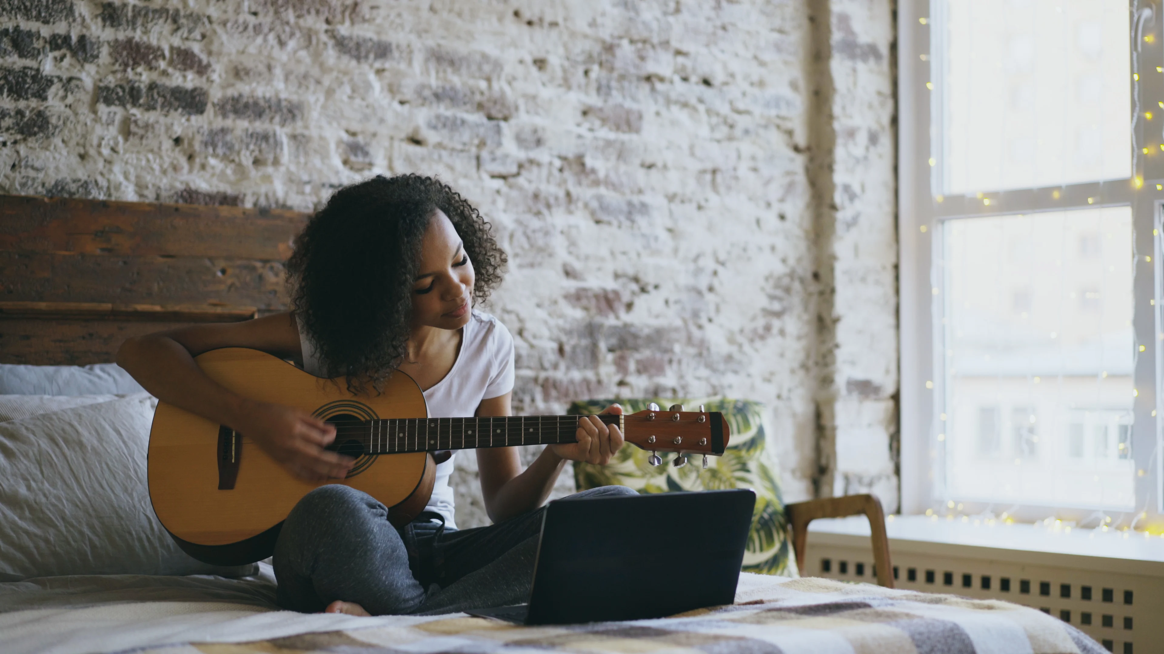 Girl sitting on a bed while playing a guitar
