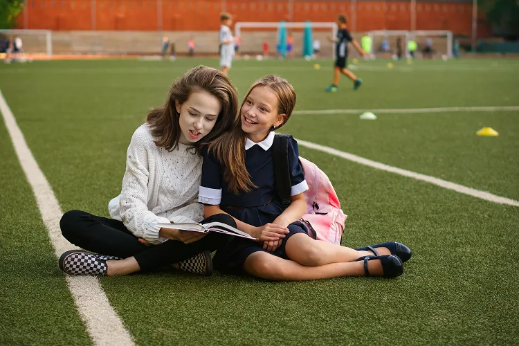 Girls reading a book while sitting on a football field