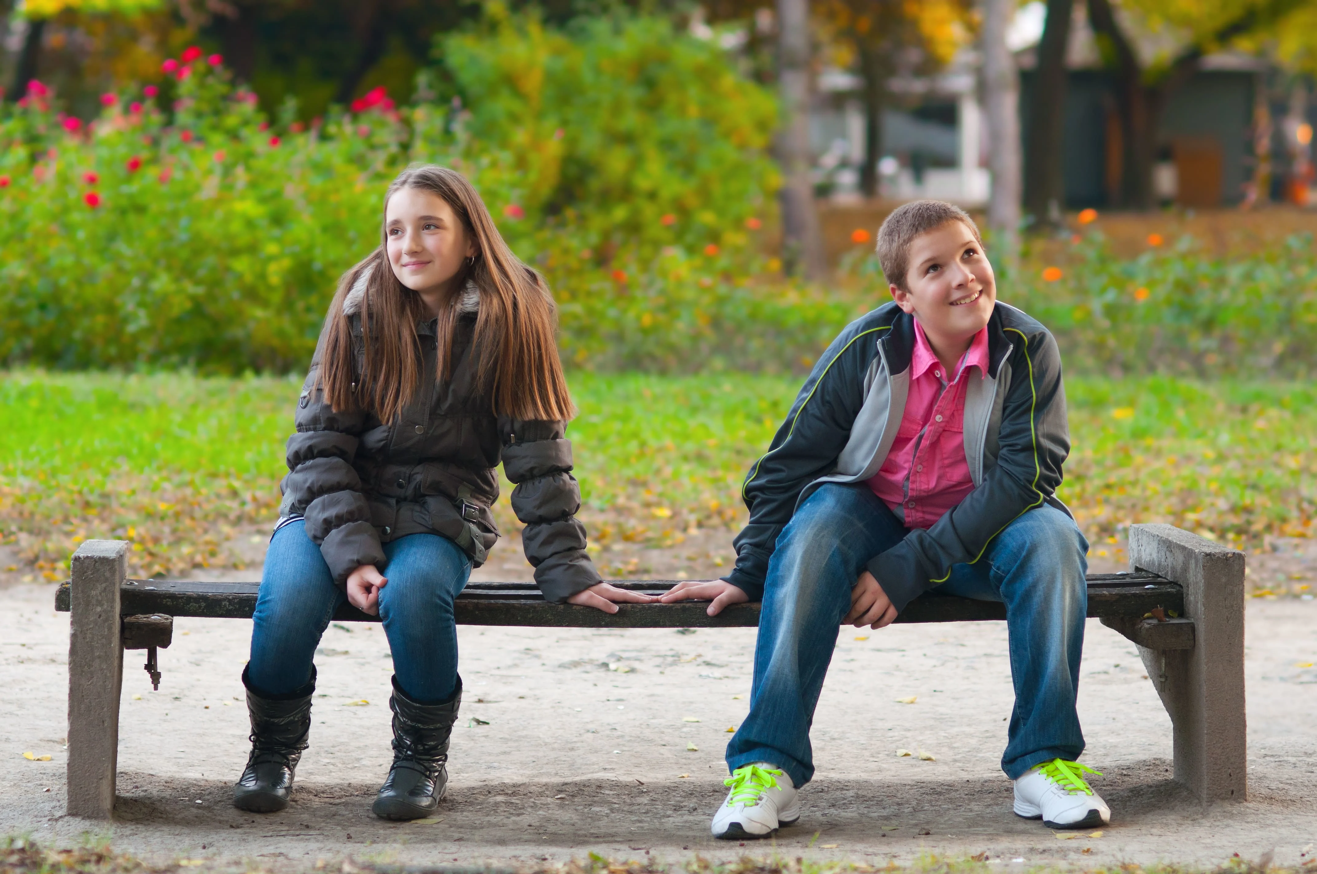 Girl and a boy sitting on a bench touching their hands while looking away