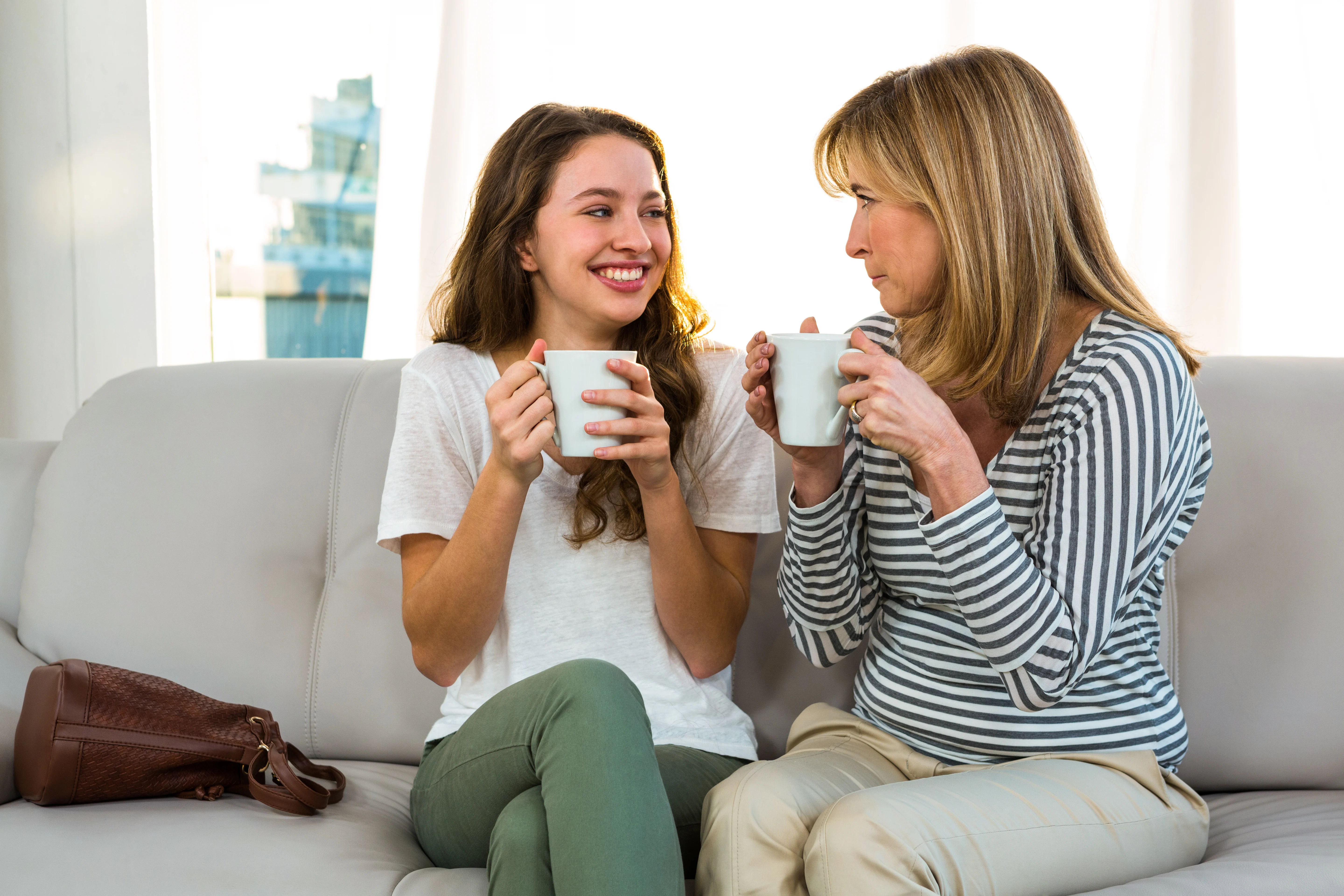 Daughter and mother sitting on a couch and looking at each other while drinking tea