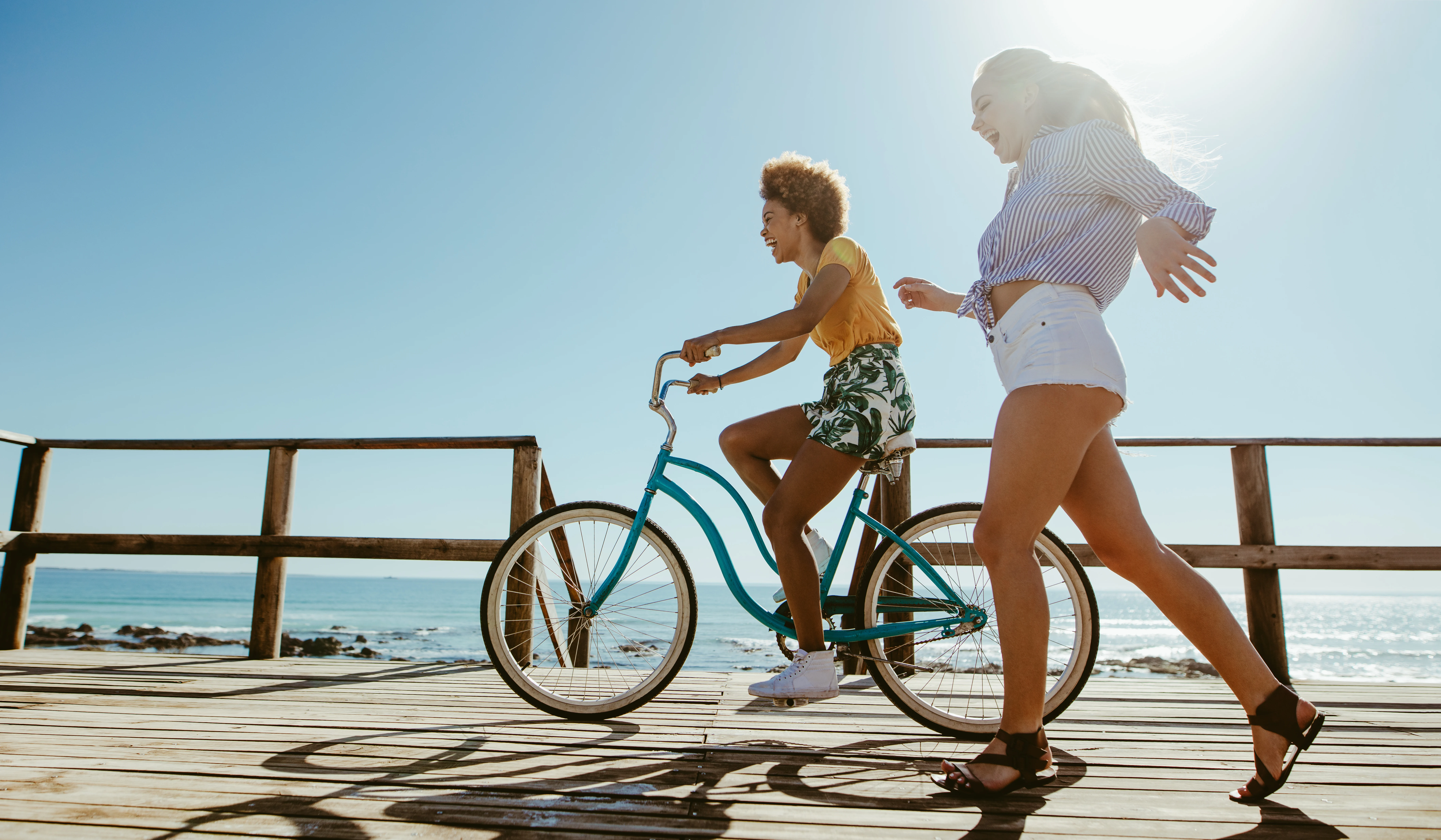 Woman riding a bike on the seashore and other woman walking next to her