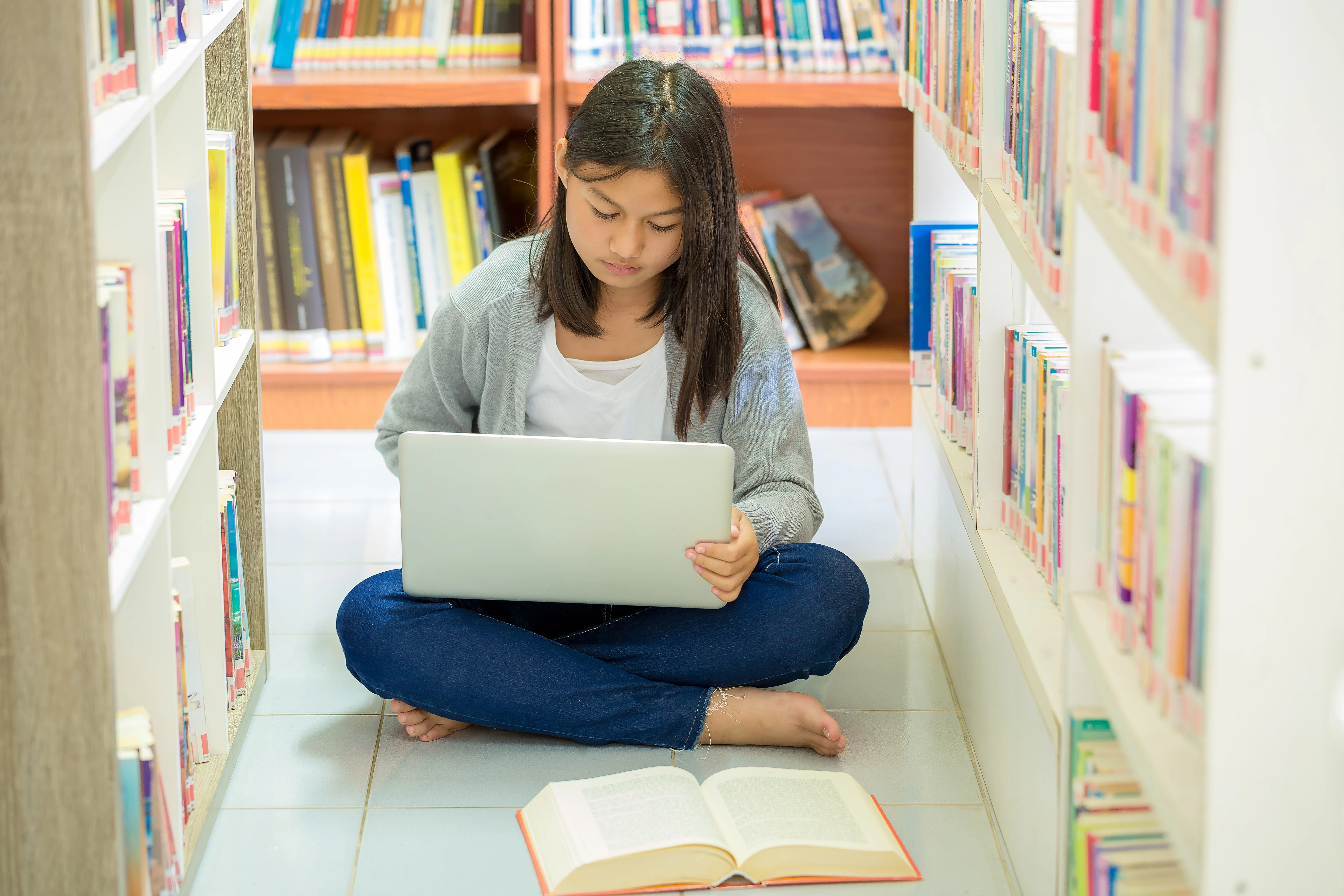 Girl sitting at the floor of a library and looking at her laptop