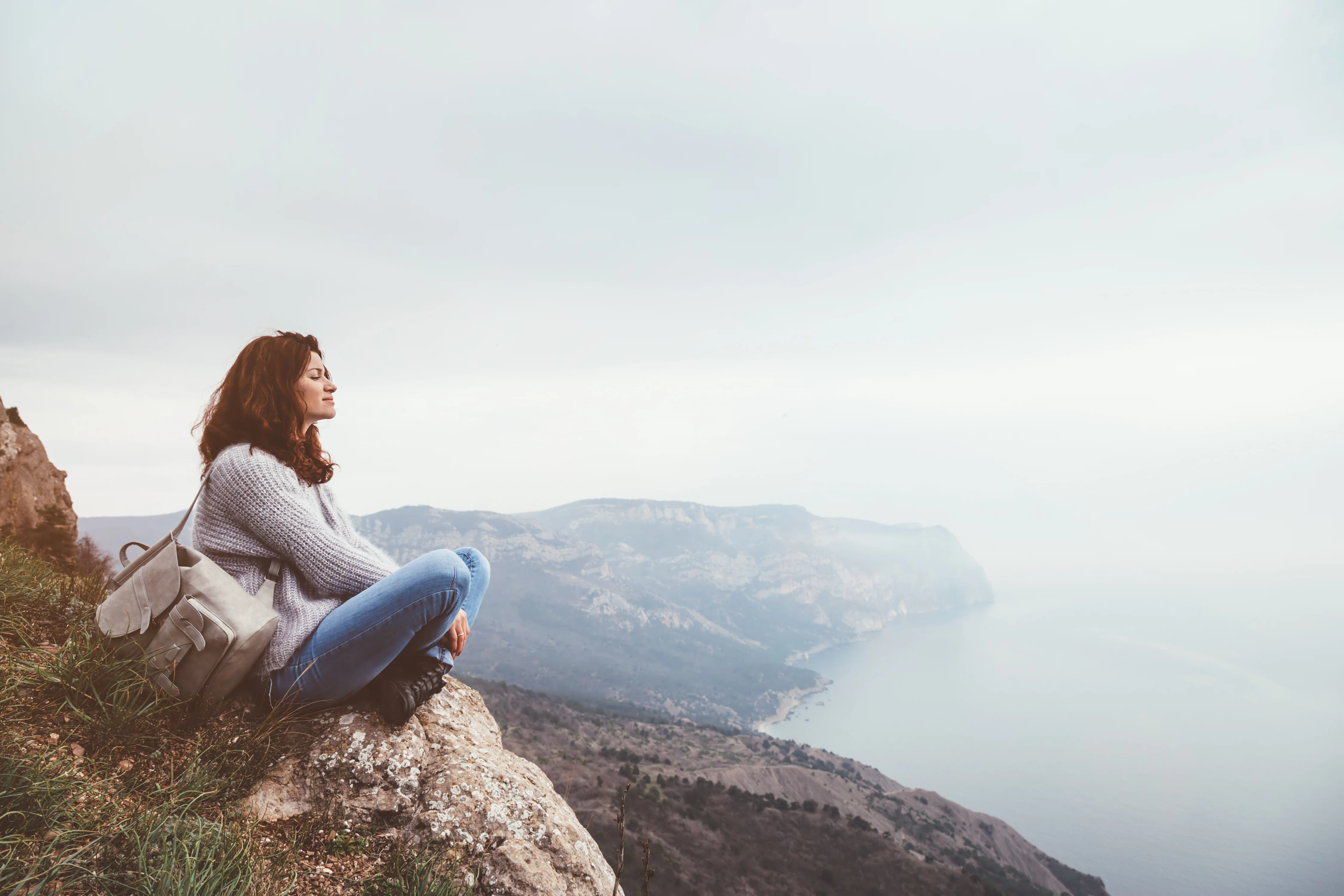 Woman sitting at the top of a rock and looking at the sea