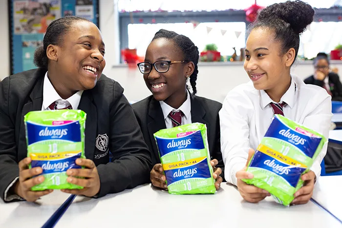 Girls sitting at a desk and holding Always Sanitary Pads packaging