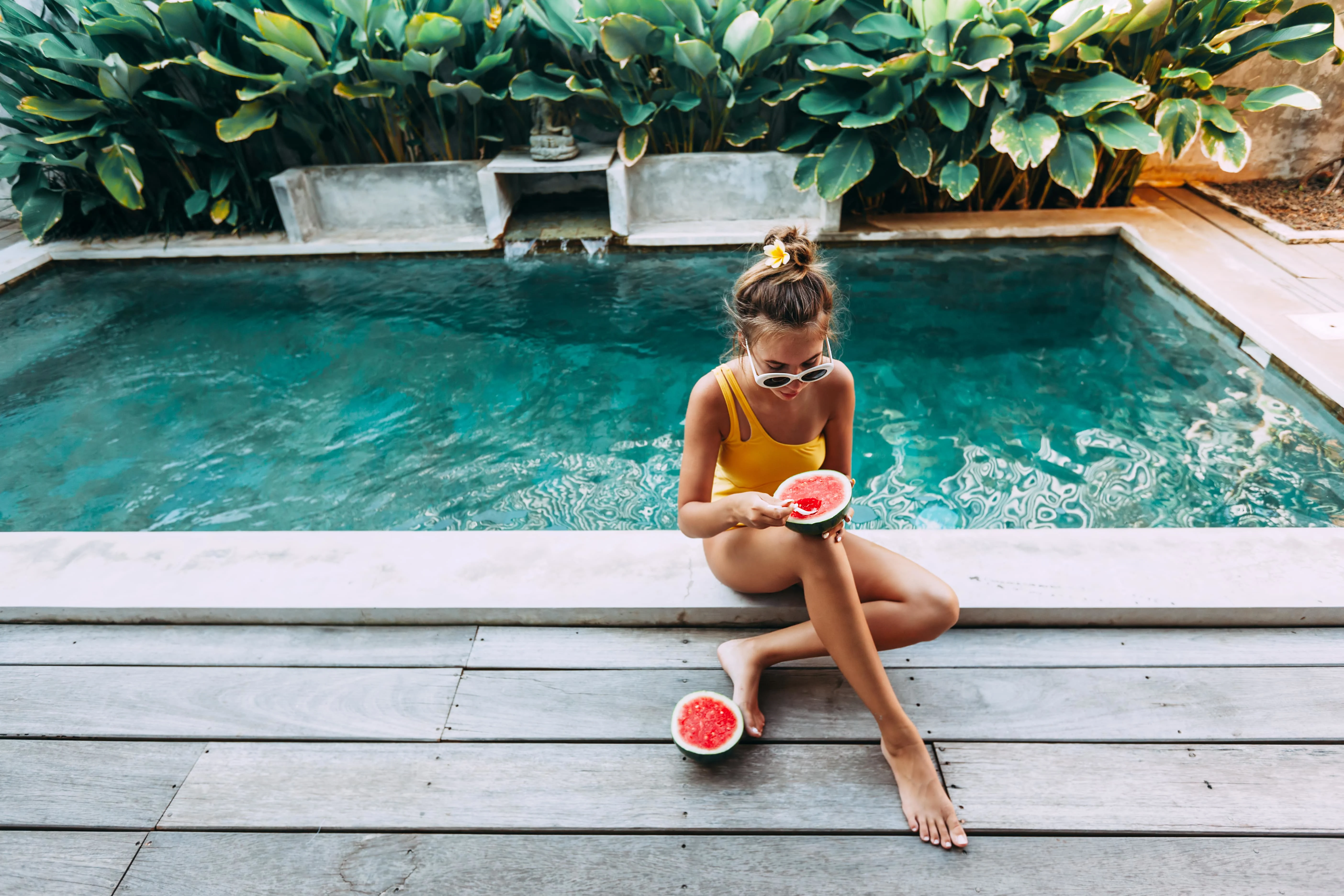 Girl eating a watermellon while sitting next to a pool