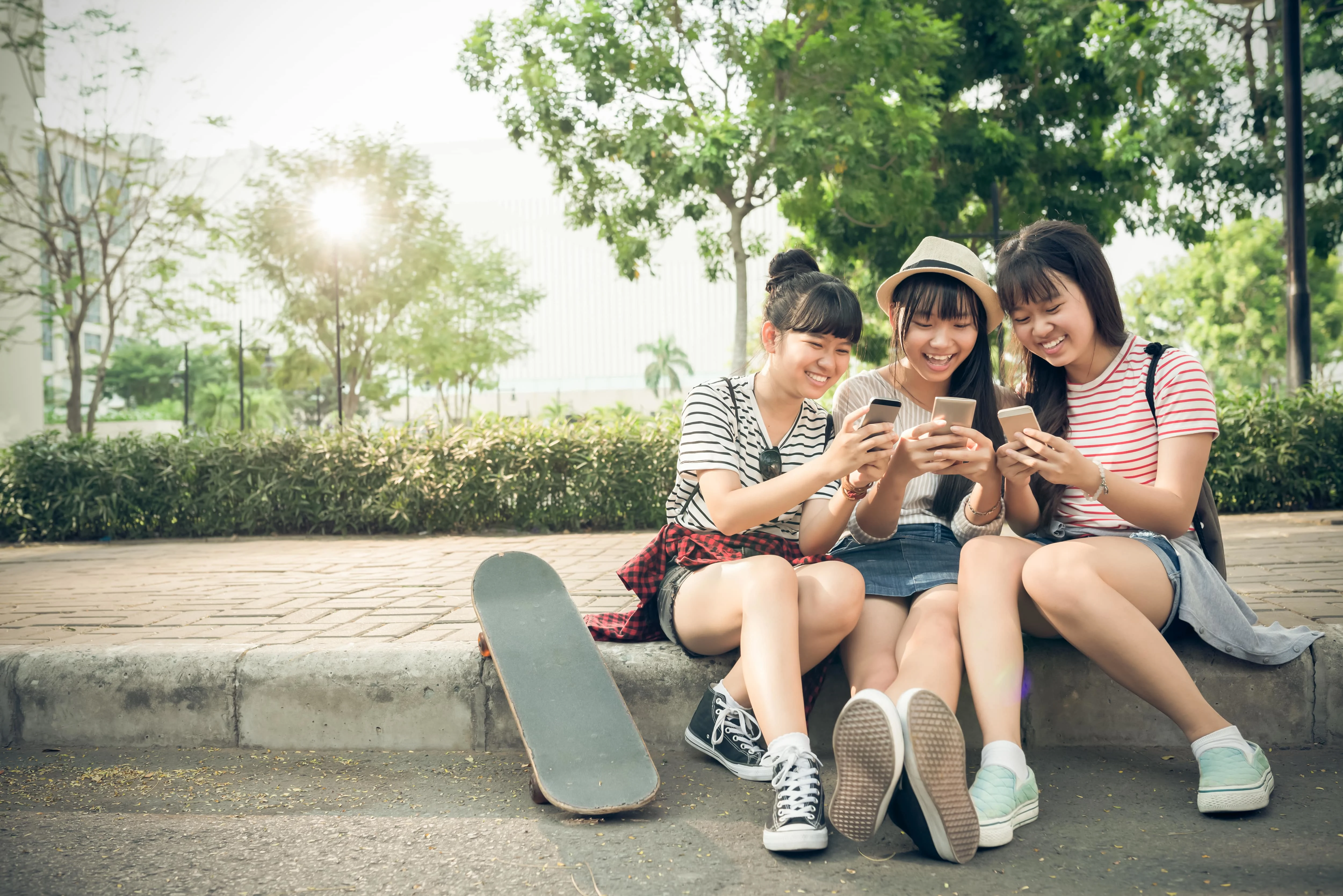 Three girls sitting on a sidewalk and looking at their phones