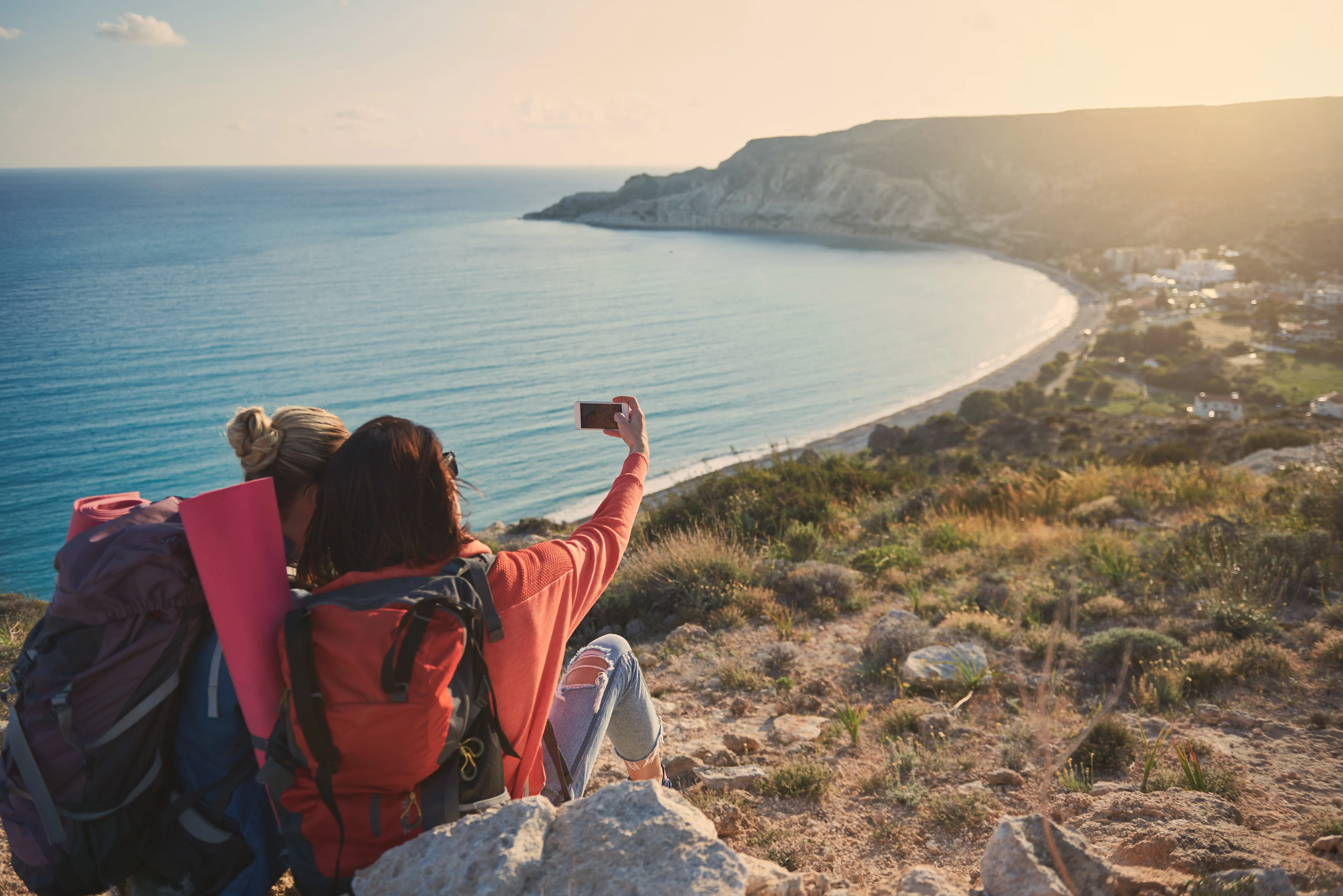 Two women sitting on the rock on the seaside while taking a photo