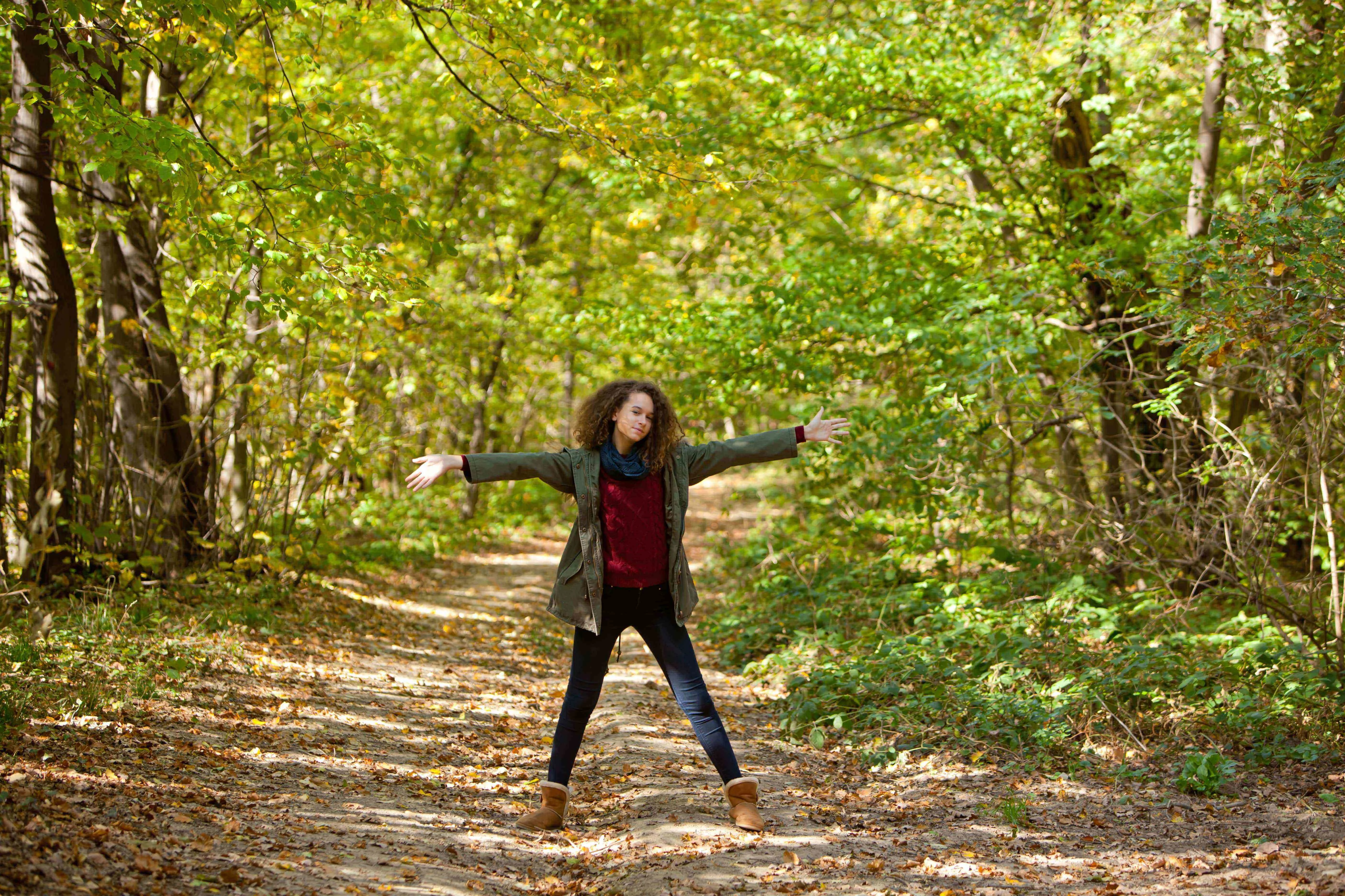 Woman standing in a autumn forest pathway with her arms wide open